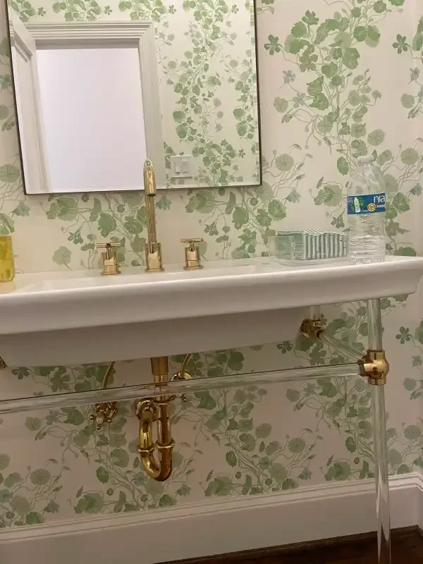 Wall-mounted brass faucets on a floral-papered powder room wall