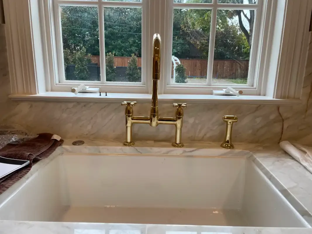 Undermount kitchen sink with a tall brass bridge faucet at a window