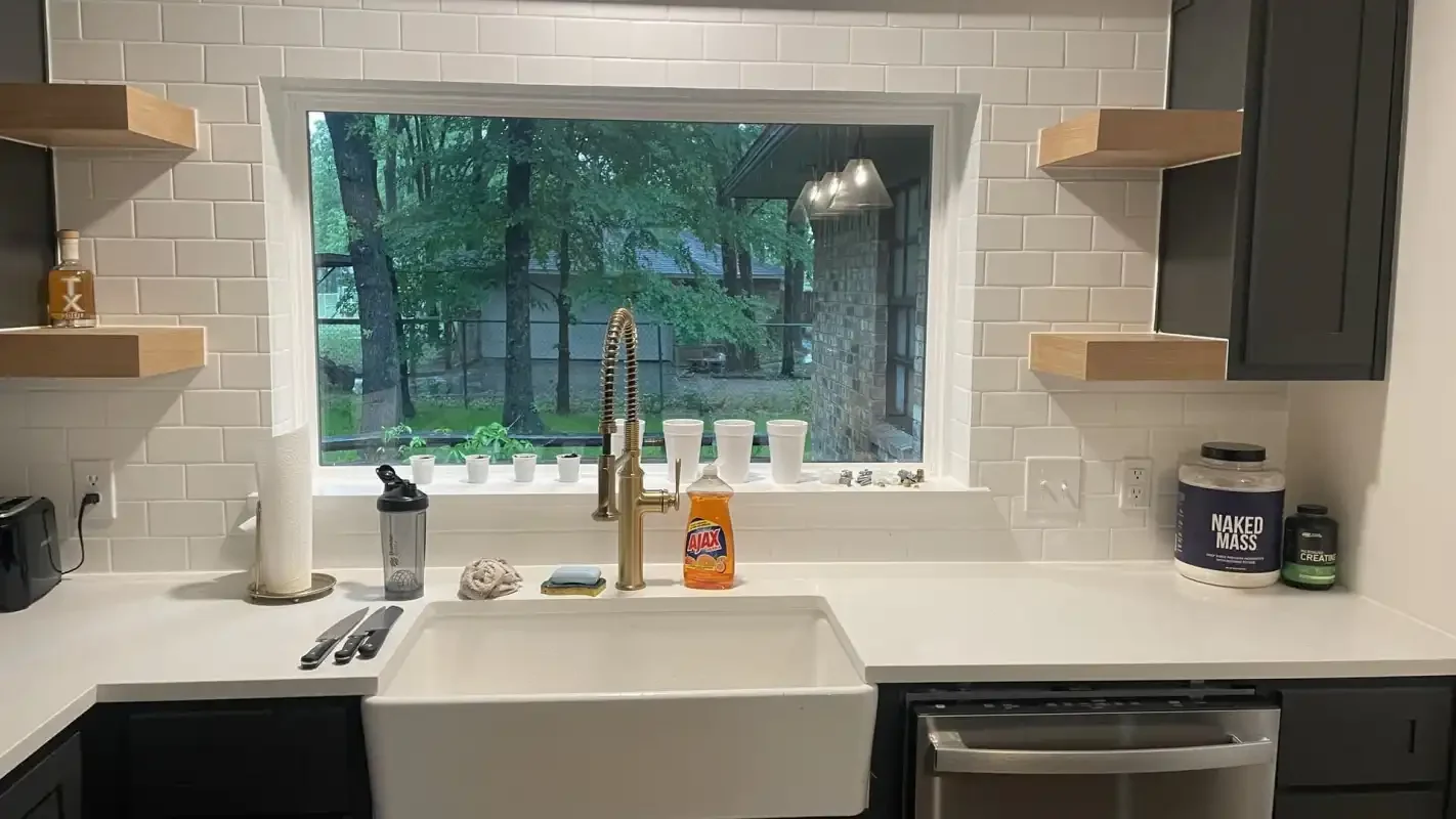Farmhouse apron sink with a brass faucet under a kitchen window