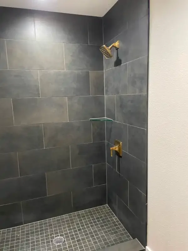Slate-tiled shower with brass shower head and mosaic floor