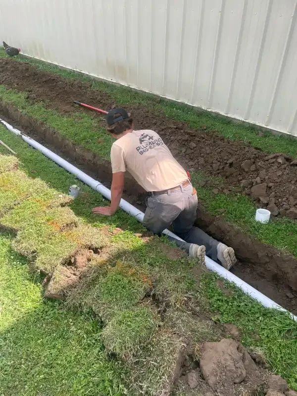 A+ Plumbing tech laying line in a trench along a fence