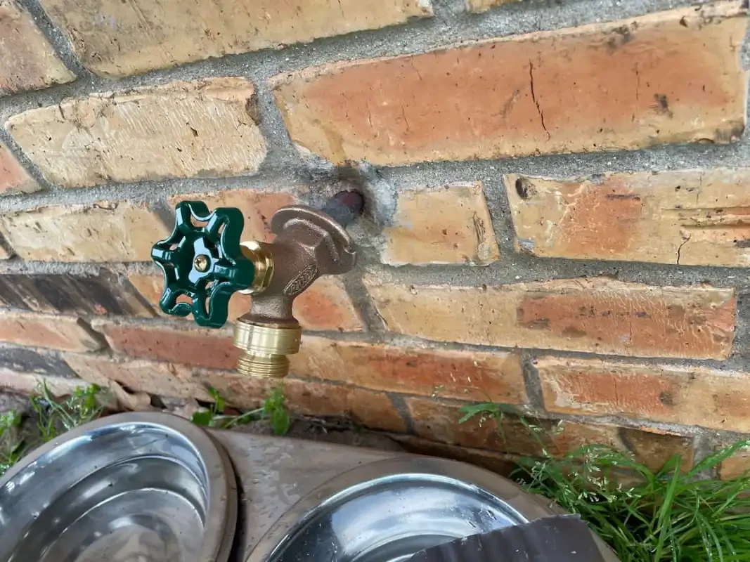 Hose bibb and supply piping at an exterior brick wall